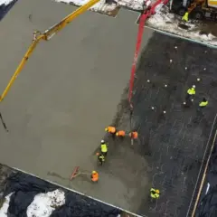 Pracownicy wylewają beton na zbrojenie, tworząc płytę fundamentową. Widać pompy do betonu i narzędzia do wyrównywania.