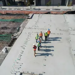 Grupa budowlańców na placu budowy. Zastanawiają się, ile kosztuje gruszka betonu, patrząc na zbrojenie i wylany fundament.