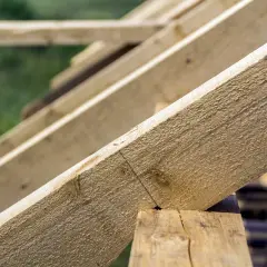 Drewniane krokwie tworzą konstrukcję dachu. Widać połączenie krokwi w kalenicy, gotowe do dalszych prac budowlanych.