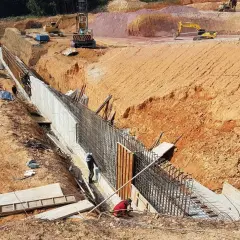 Budowa muru oporowego, gdzie pracownicy przygotowują zbrojenie. Widać koparki i wykop. To kluczowy etap, by wiedzieć, ile potrzeba betonu na fundamenty.