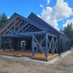 Szkielet domu kanadyjskiego z drewnianym tarasem i szarymi, geometrycznymi podporami.