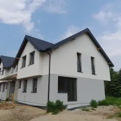 Nowy, dwukondygnacyjny dom jednorodzinny wolnostojący w stanie surowym, z szarym dachem i dwukolorową elewacją.