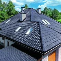 Elegancki rzut dachu dwuspadowego z ciemnej dachówki, z kilkoma oknami połaciowymi i dwoma kominami, otoczony zielenią.