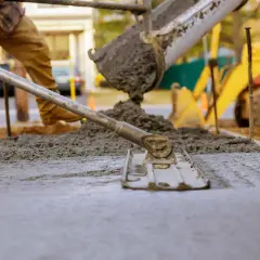 Robotnicy wylewają beton, który wiąże, tworząc nową nawierzchnię. W tle widać koparkę.