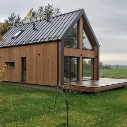 Nowoczesne projekty domów z drewna, z dużymi przeszkleniami i tarasem, otoczone jesienną przyrodą.