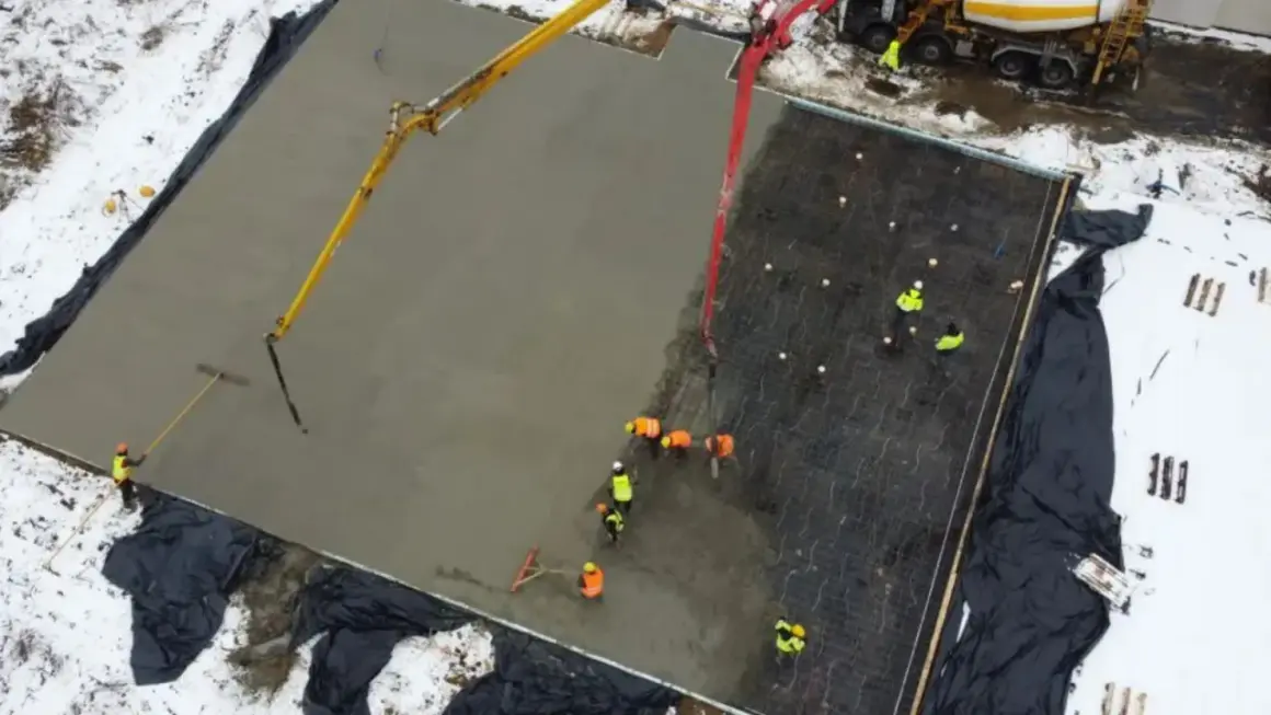 Pracownicy wylewają beton na zbrojenie, tworząc płytę fundamentową. Widać pompy do betonu i narzędzia do wyrównywania.
