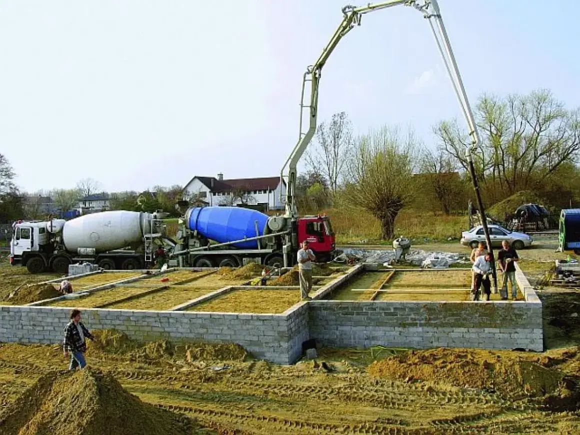 Betonowanie ławy fundamentowej. Dwie betoniarki i pompa do betonu pracują na budowie.