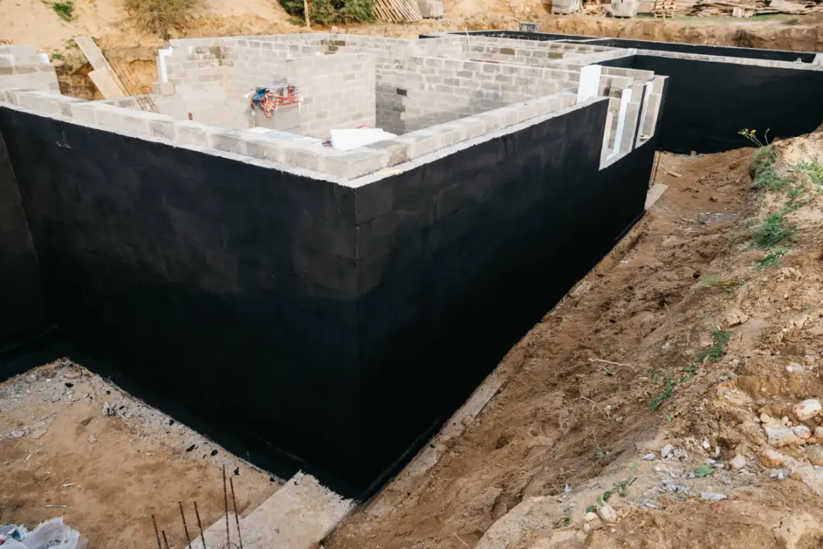Budowa piwnic: wylana płyta fundamentowa, ściany z bloczków betonowych pokryte czarną izolacją przeciwwilgociową.