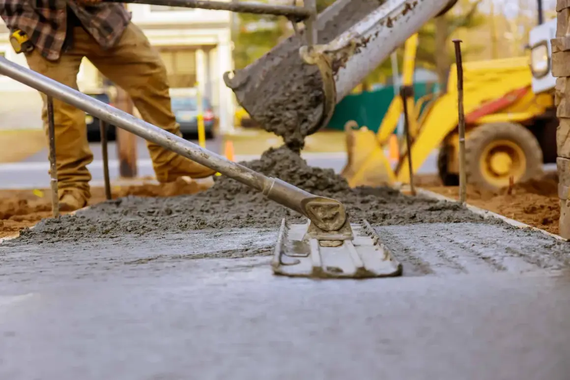Robotnicy wylewają beton, który wiąże, tworząc nową nawierzchnię. W tle widać koparkę.
