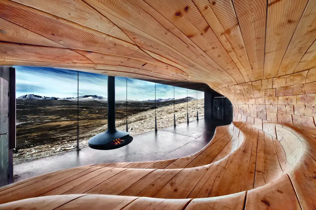 Nowoczesne zastosowanie drewna w budownictwie: zakrzywione drewniane ławy i ściany tworzą przytulne wnętrze z widokiem na góry.