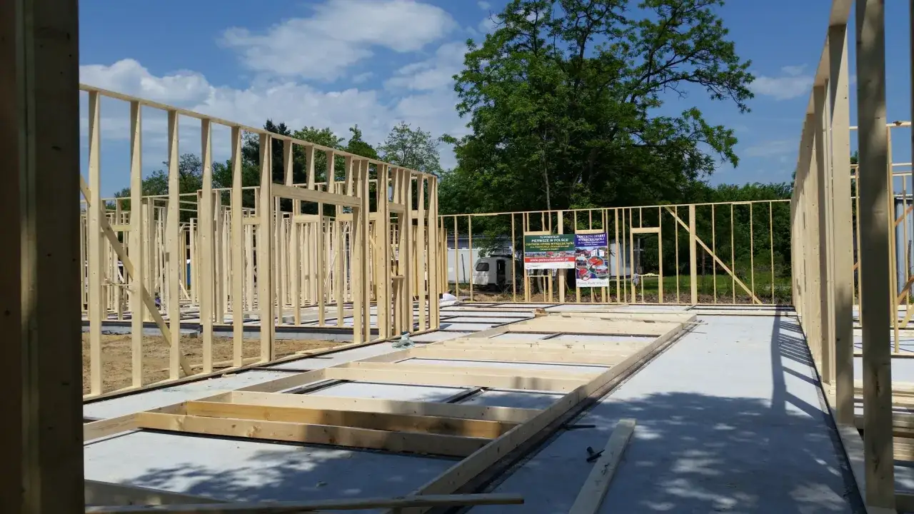 Widok na budowę domu drewnianego. Szkielet ścian i stropu z belek drewnianych na betonowym fundamencie.