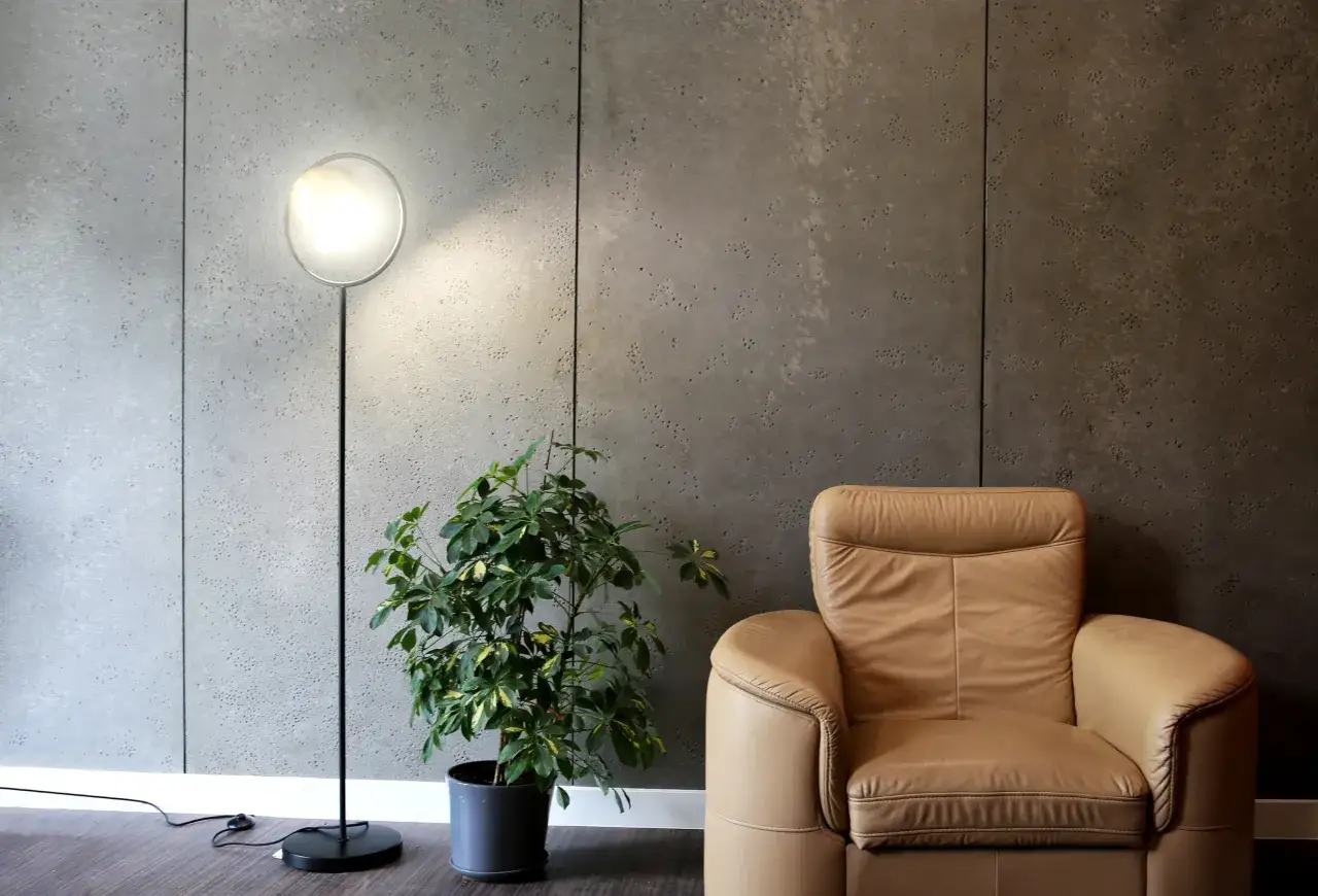 Nowoczesne wnętrze z betonem architektonicznym na ścianie, skórzanym fotelem i designerską lampą. Inspiracja, jak położyć beton architektoniczny.